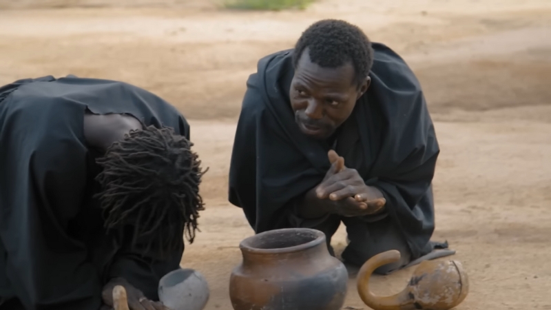 Two People in Traditional Clothing Perform a Ritual with Pots and Tools on The Ground
