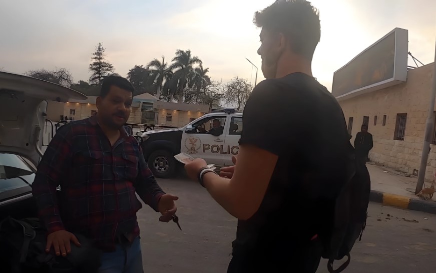 A man in a plaid shirt exchanges money with a taxi driver