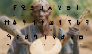 N’Ko alphabet characters overlaid on an image of a traditional West African drummer