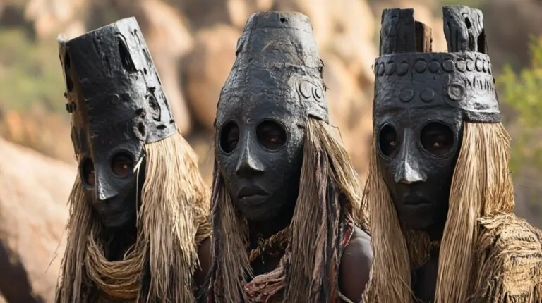 Three Dogon people wearing traditional black wooden masks with straw details during a ritual
