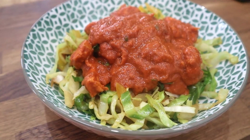 Moambe Chicken served over sautéed cabbage in a patterned bowl, topped with a thick, rich red sauce