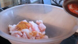 Raw, diced chicken in a plastic bowl being seasoned with spices before cooking