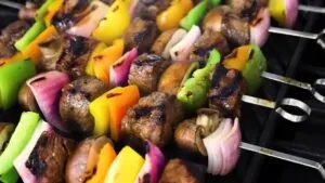 Grilled Shish Kabobs with beef, bell peppers, onions, and mushrooms cooking on metal skewers over open flame