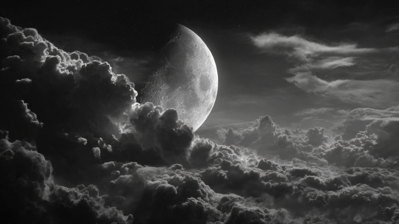 Half moon shining through thick clouds in the night sky over rural West African communities