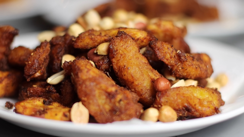 A close-up of kelewele served on a white plate, garnished with a mix of roasted peanuts