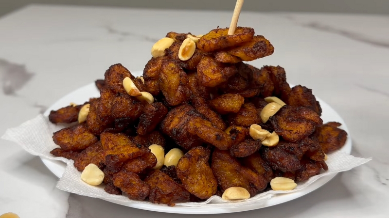 A plate of golden-brown Ghanaian kelewele served with roasted peanuts on a white paper-lined dish
