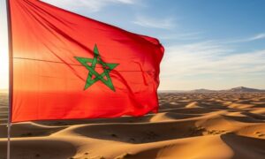 The Moroccan flag waving over the undulating Sahara landscape at sunset