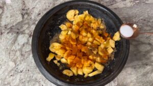 Chopped plantains are being seasoned with spices and salt in a traditional Ghanaian grinding bowl
