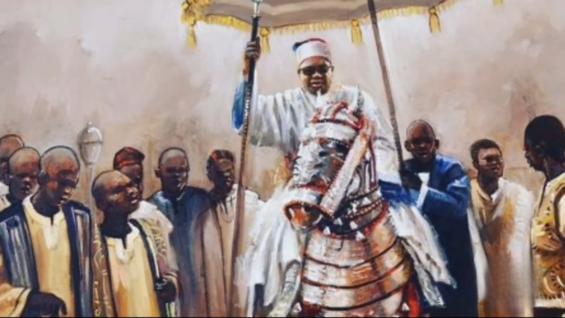 A Kanuri ruler in traditional royal attire sits on an armored horse, surrounded by attendants during a ceremonial gathering