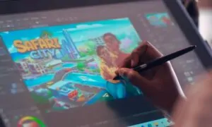 A person is using a stylus to draw on a digital tablet connected to a computer screen