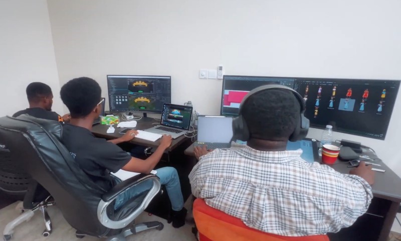 Three men seated at a desk, focused on their work with computer screens in front of them