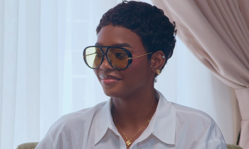 Dede Ashiogwu with short hair smiles while wearing large tinted sunglasses and a white shirt