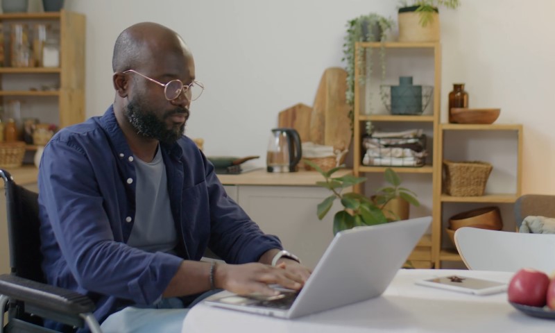 A man in glasses uses a laptop at a table, appearing focused