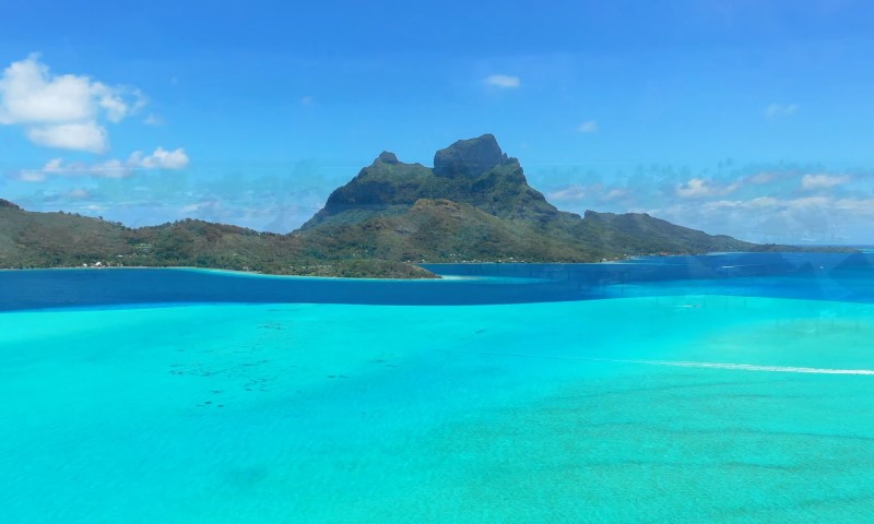 Crystal-clear turquoise sea with gentle waves in the foreground, lush green hills