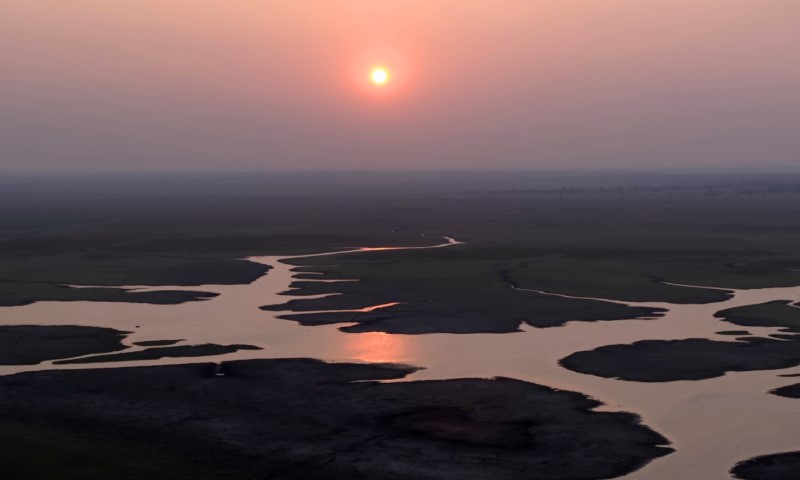 A serene sunset over a vast landscape with winding water channels reflecting the sun