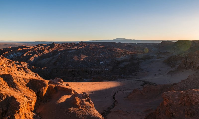 Sunset over a vast, Atacama desert landscape with red-hued formations and distant mountains