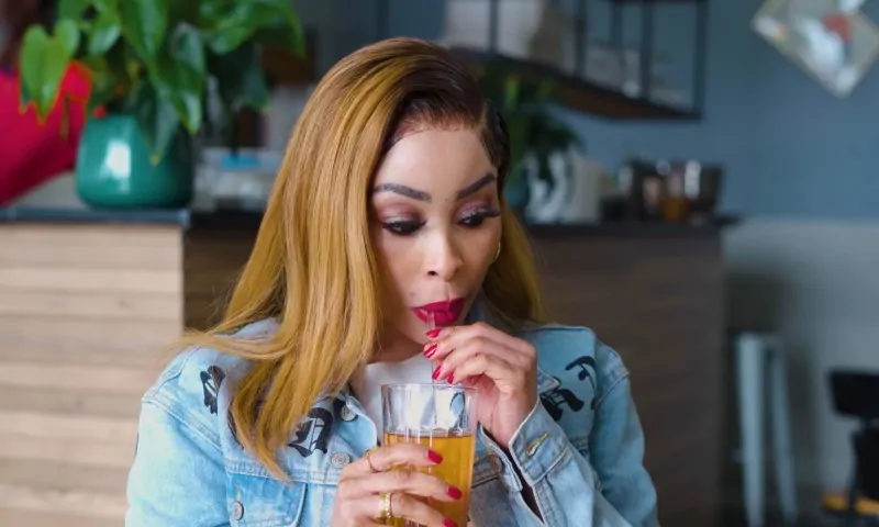 Khanyi Mbau sips orange juice through a straw in a glass