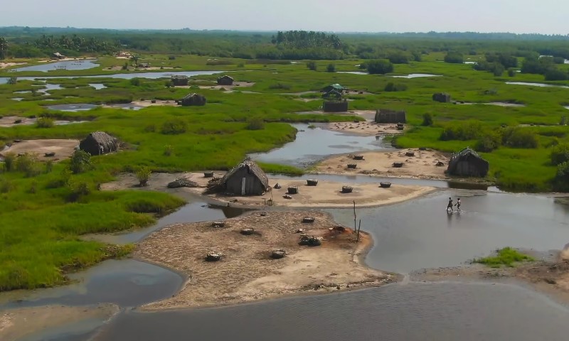 Aerial view of a serene, lush green landscape dotted with small huts on sandy patches