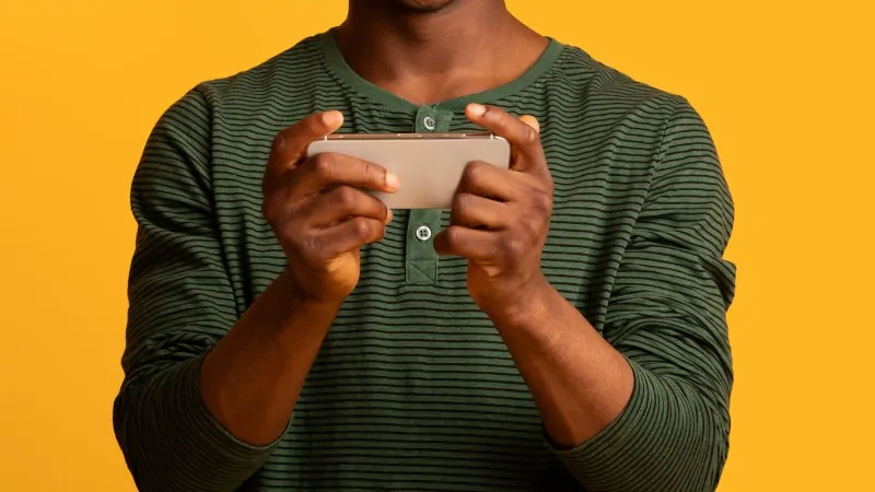 A man holds a smartphone horizontally while playing an online mobile game