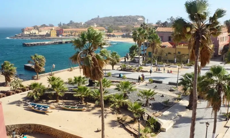 Scenic coastal view of a vibrant village with colorful buildings, palm trees, and small boats on sandy shores