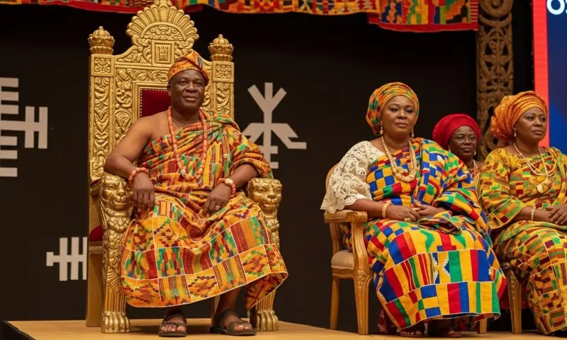 A man and three women in vibrant kente cloth sit on ornate chairs