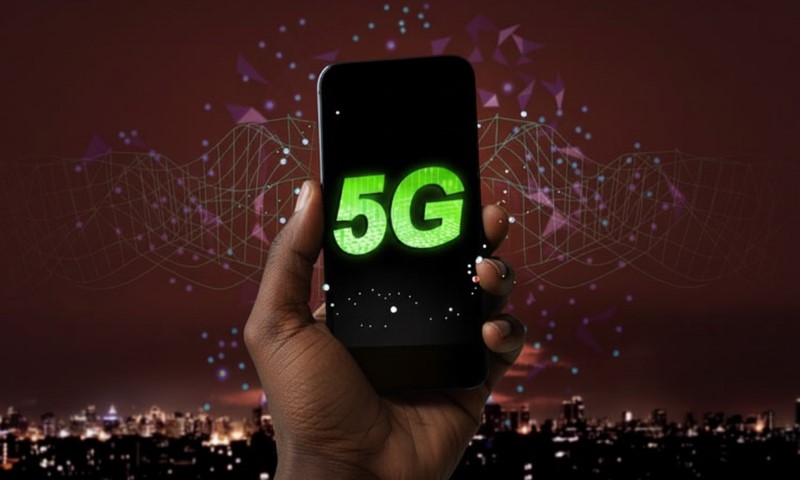 A hand holds a smartphone displaying "5G" in bright green, against a backdrop of a city skyline at night