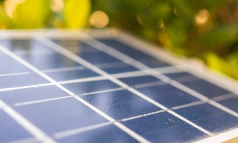 Close-up of a solar panel with reflective blue grid patterns, partially in focus