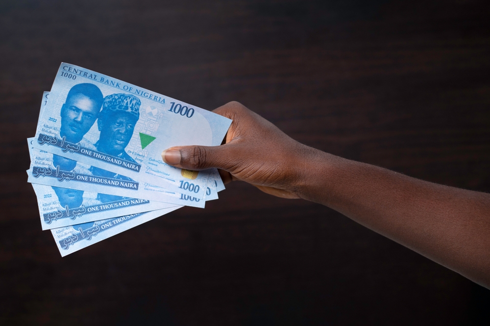 A hand holds several Nigerian one thousand naira notes against a dark background